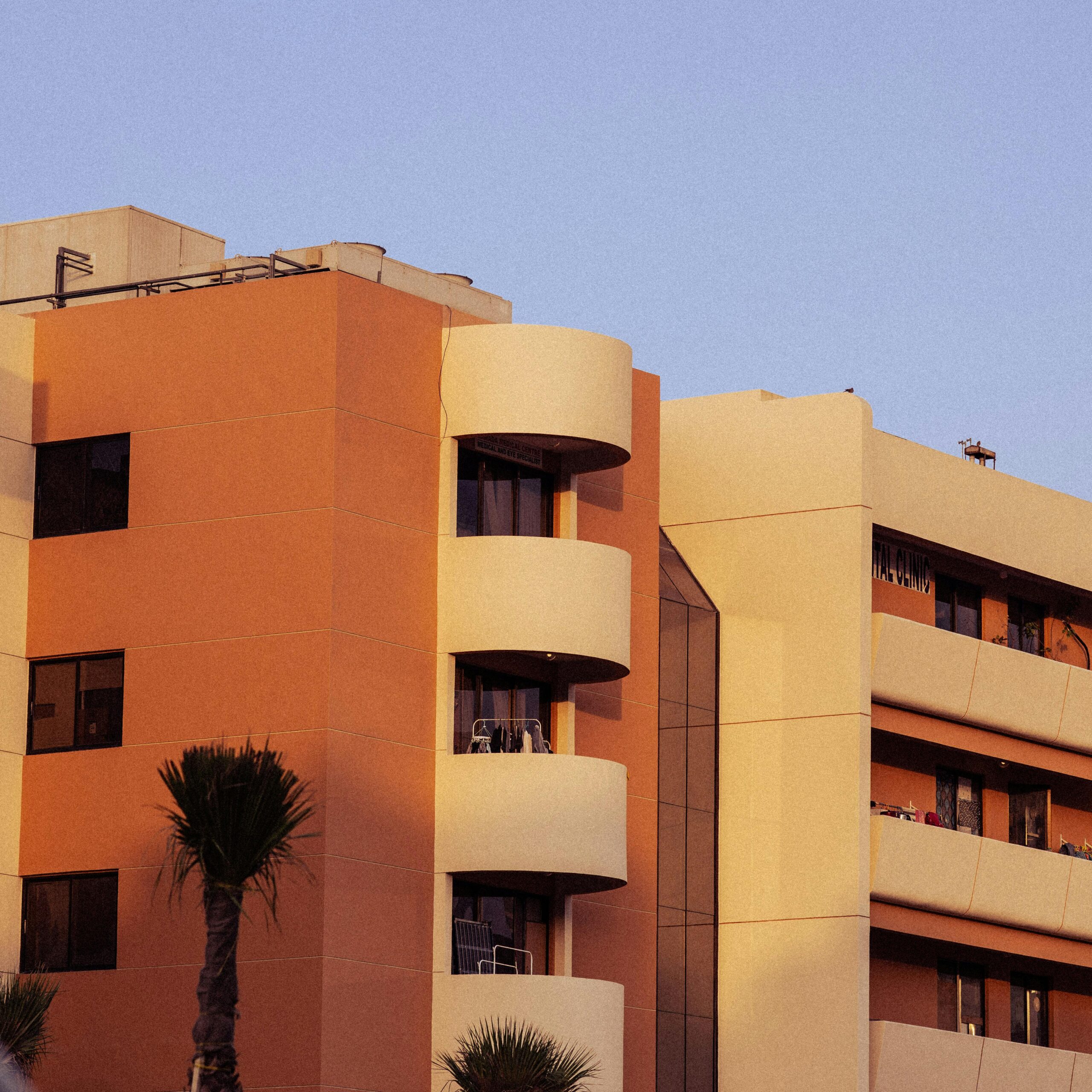 Contemporary urban apartment with balconies at sunset, enhanced by palm trees.