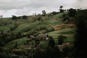 Charming rural landscape featuring lush green hills and rustic cottages under a cloudy sky.